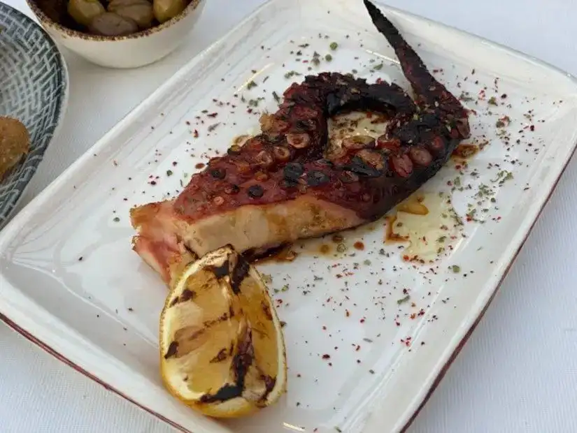 A delectable close-up of grilled seafood at Yengec Restaurant, showcasing a plate of freshly grilled octopus, lemon wedges, and seasonings.