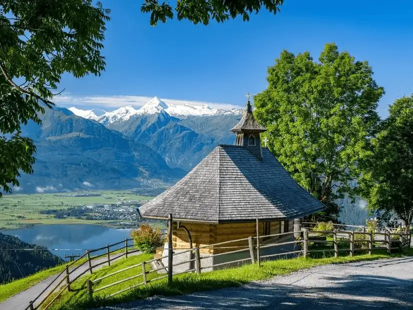 A picturesque view of a quaint wooden chapel with mountains in the background.