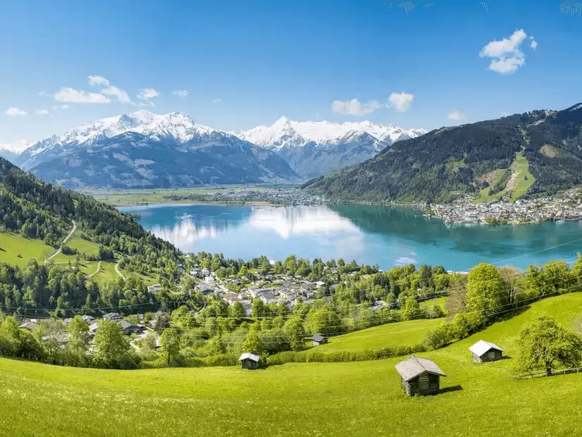 A panoramic view of a serene lake surrounded by mountains and green fields.