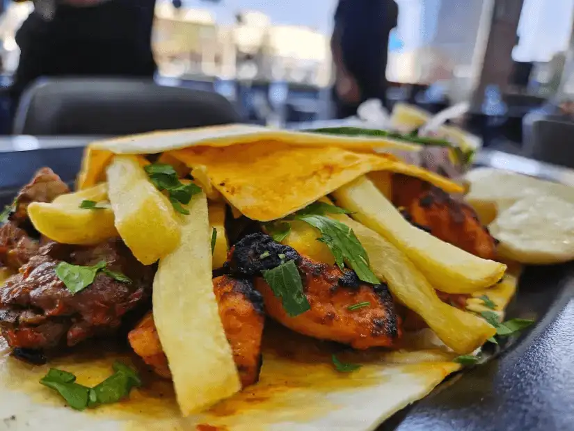 A flavorful dish with grilled meat, fries, and wrapped in soft flatbread, garnished with fresh herbs.
